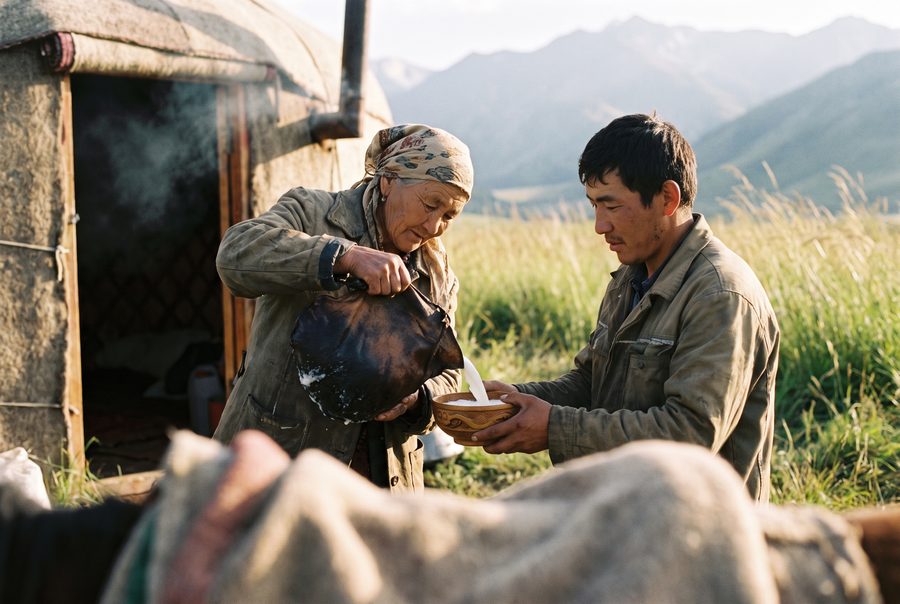 A wooden bowl of kymyz offered in front of a yurt